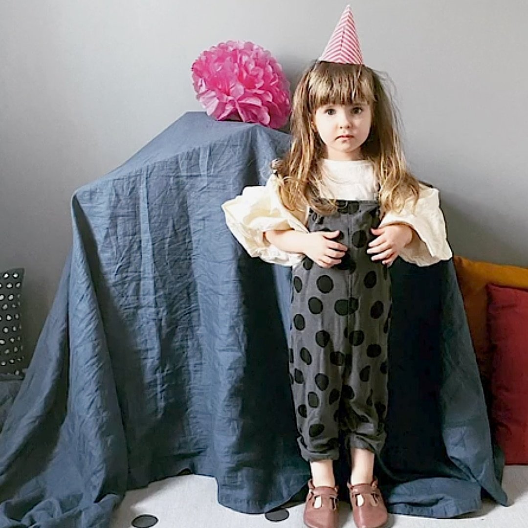 Girl in a birthday hat standing before a large wooden dollhouse covered with fabric as a gift surprise