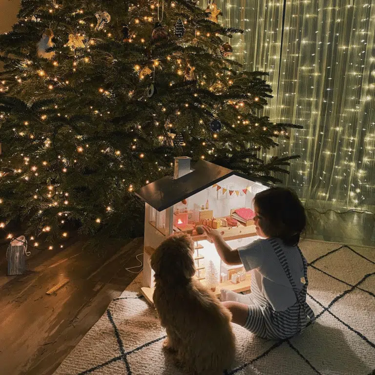 A cozy Katin Domik dollhouse with glowing lights near a Christmas tree with a child and a dog.